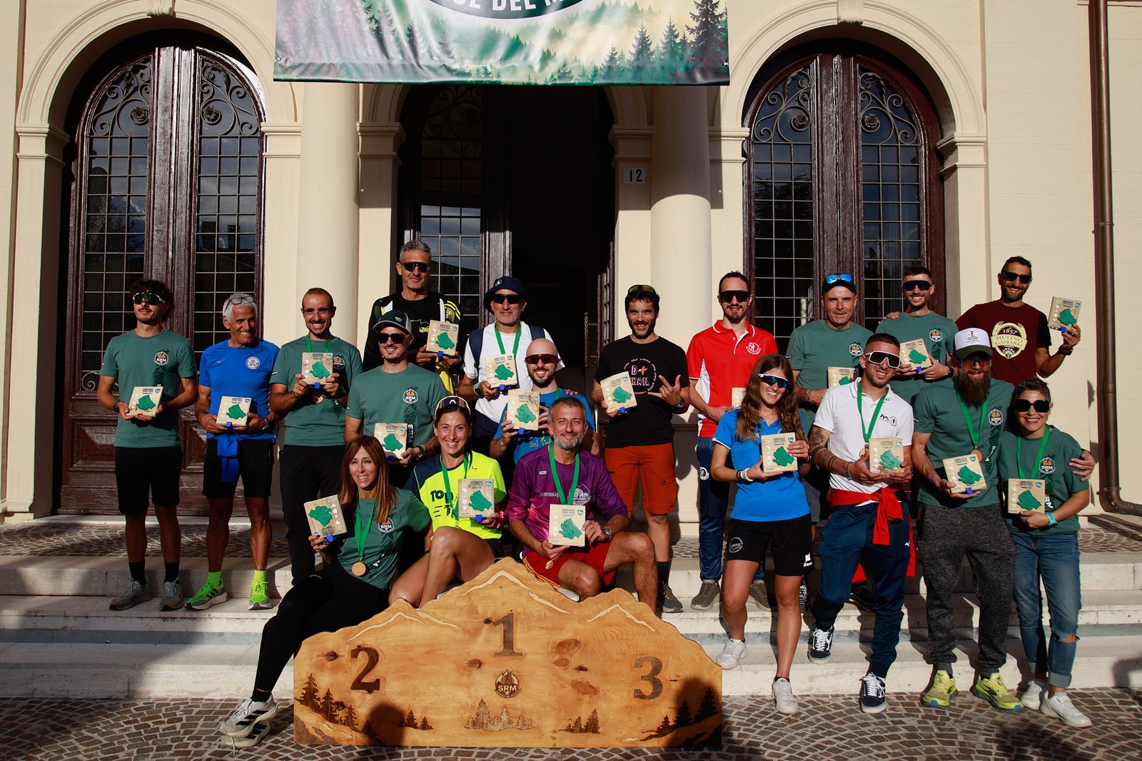 I finisher del circuito Abruzzo Trail Run Series in posa davanti al Municipio con il podio in legno