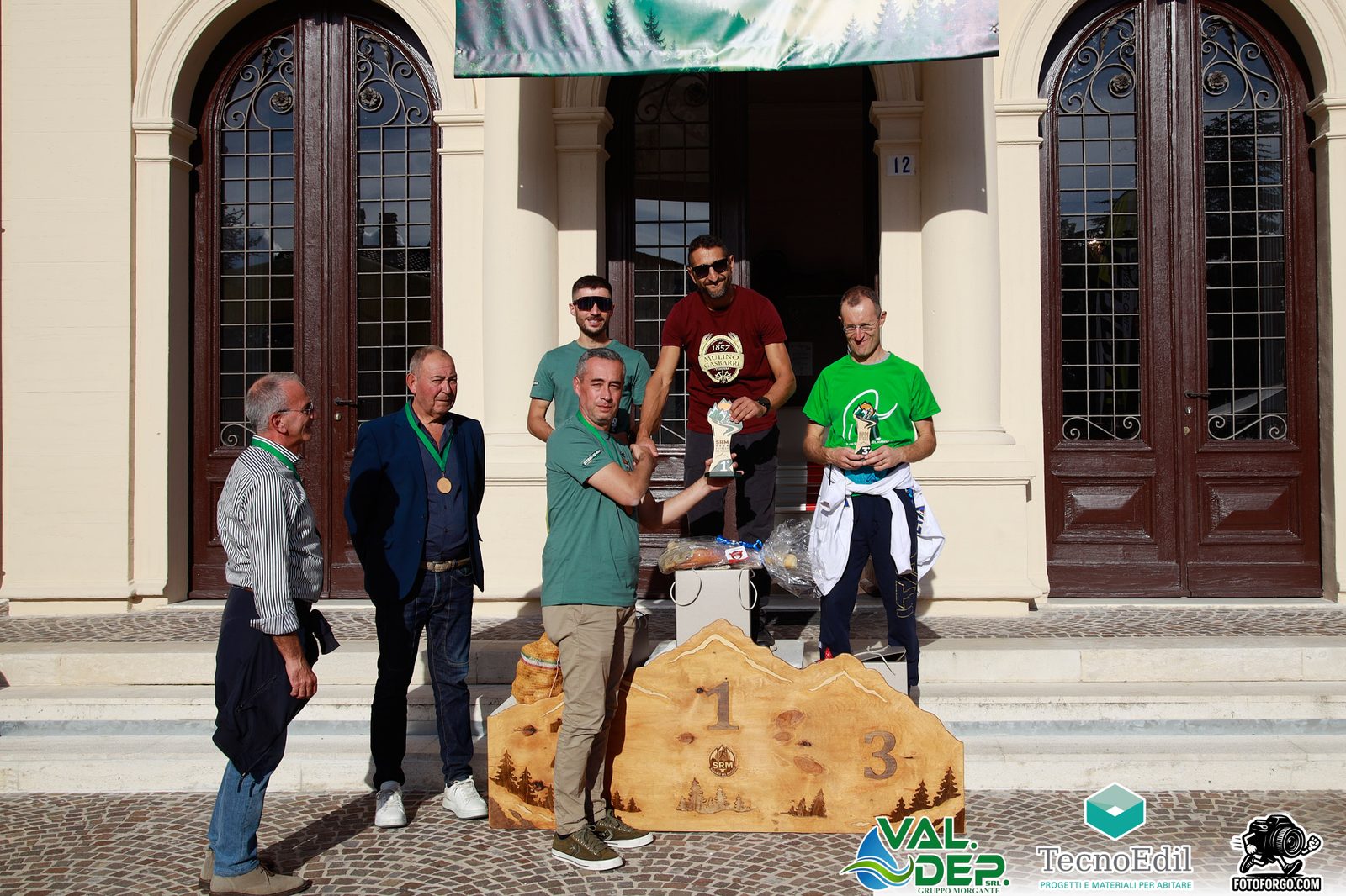 Il podio assoluto maschile della Skyrace del Maglio 2026 davanti al Municipio, con il podio in legno intagliato